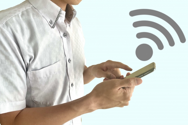 スマートフォンを操作する人と無線通信を示すアイコンのイメージ画像