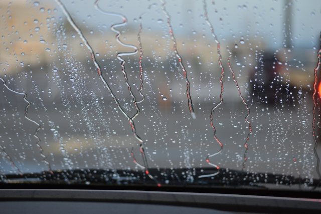 雨の中を走行する車のフロントガラス越しの景色。水滴が残り視界がぼやけている様子。