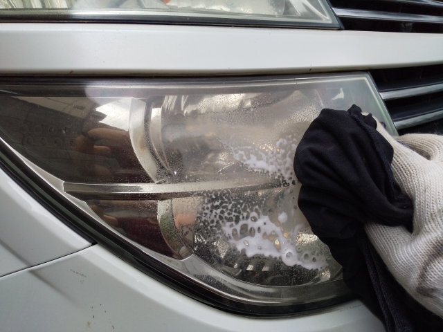 ヘッドライトにクリーナーを塗り、泡立てながら磨いて黄ばみを落としている様子。手袋をして丁寧に作業している。