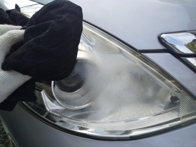 車のヘッドライトをクロスで磨き、黄ばみを落としている様子。透明感を取り戻すためのメンテナンス作業。