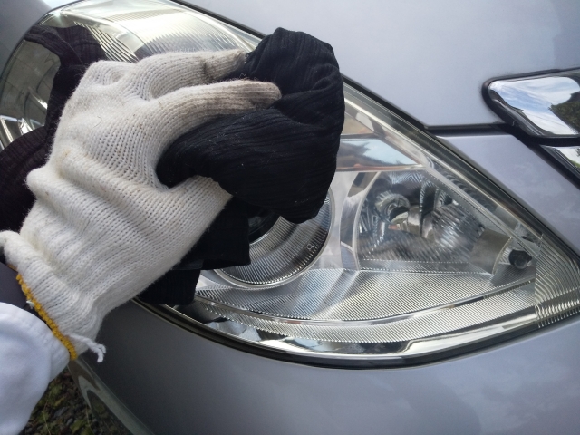 クロスでヘッドライトの表面を拭き取り、黄ばみを落としている様子。手袋をして丁寧に磨いている。